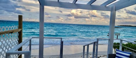 A beach view from a covered area with a railing, a bench, and a view of the ocean.