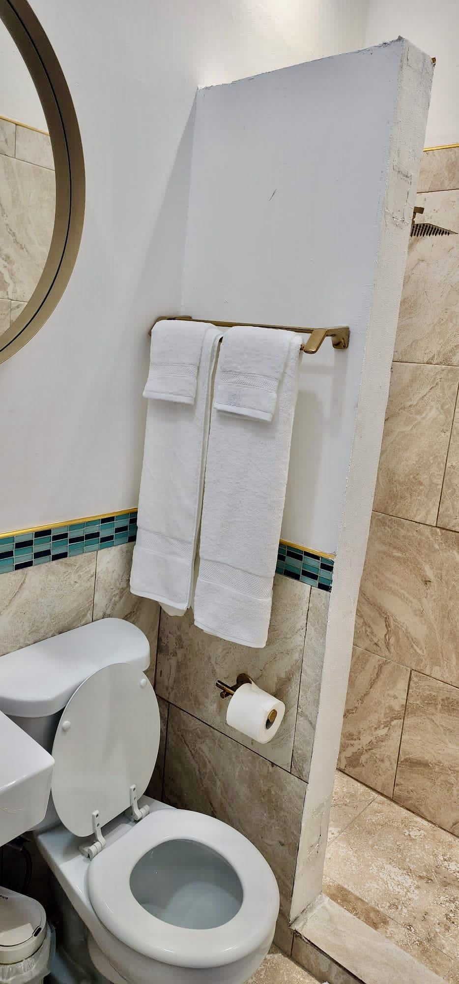 Un baño con un inodoro, un rollo de papel higiénico y dos toallas colgadas en un perchero.