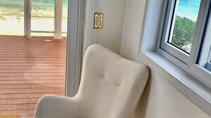 A room with two plush armchairs, a patterned rug, a bottle of wine, and a view of the ocean through a large window. - The Suite Life (Rokers Point)