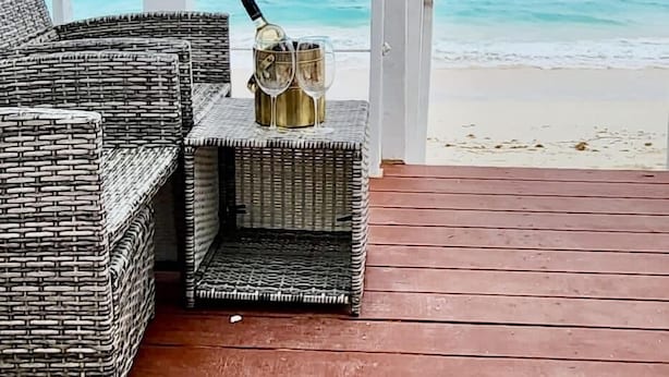 A covered outdoor seating area with wicker furniture and a view of the ocean. - The Suite Life (Rokers Point)