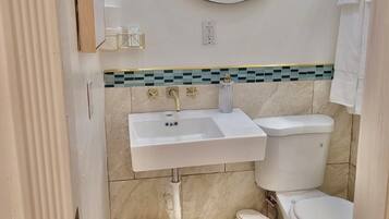 Un baño con un lavamanos blanco, un inodoro y un espejo. Hay un cesto de basura pequeño y una cesta tejida.