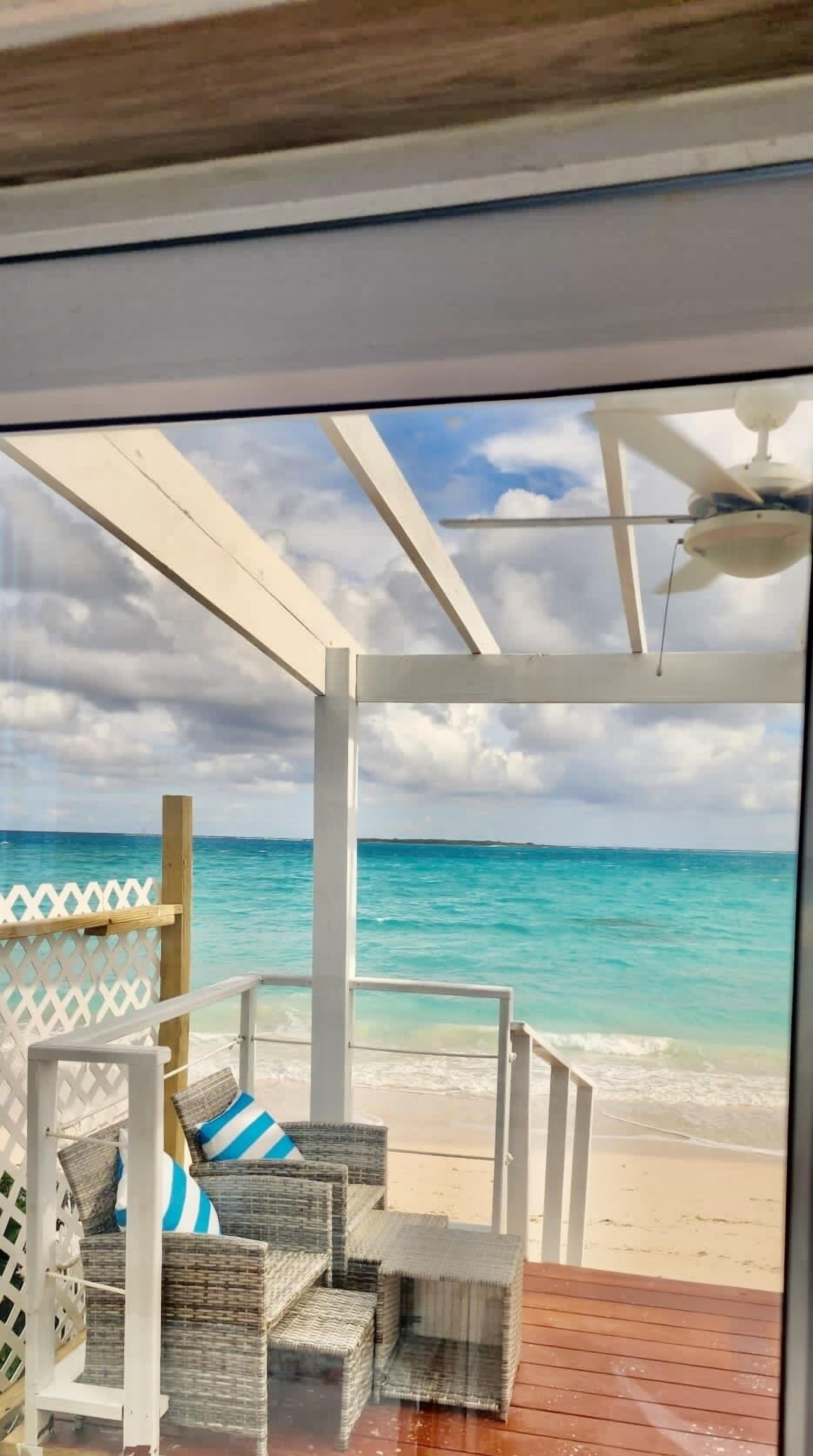 Une vue sur la plage depuis un espace abrité, aménagé avec des meubles en osier et une terrasse en bois.