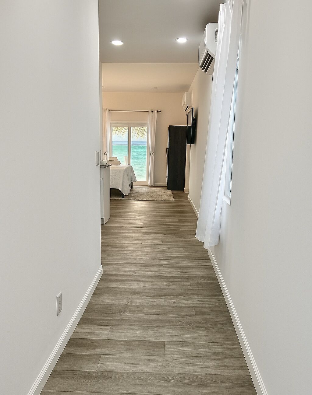 A hallway with wooden flooring, white walls, and a view of the ocean through a glass door.