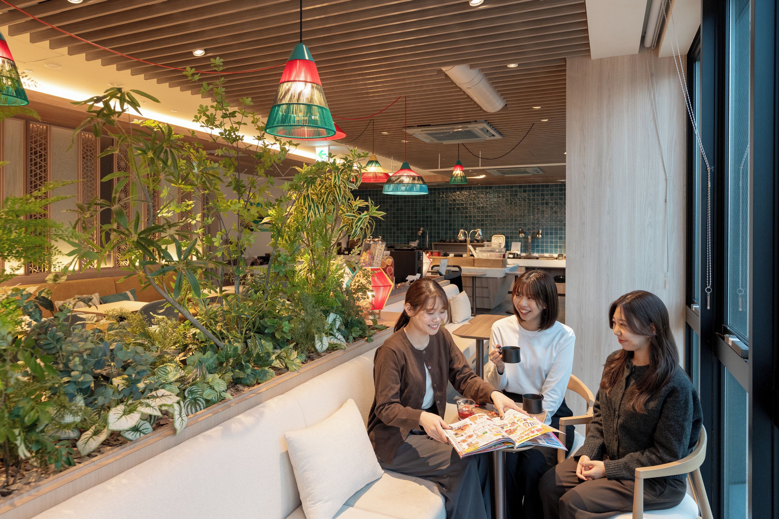 A modern indoor space with a seating area, plants, and a kitchen in the background.