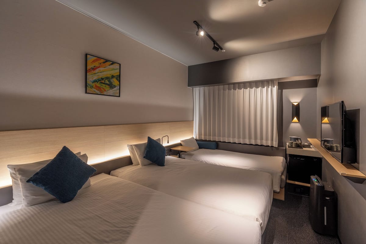 Quarto de hotel moderno com duas camas, uma escrivaninha, televisão e um quadro na parede.