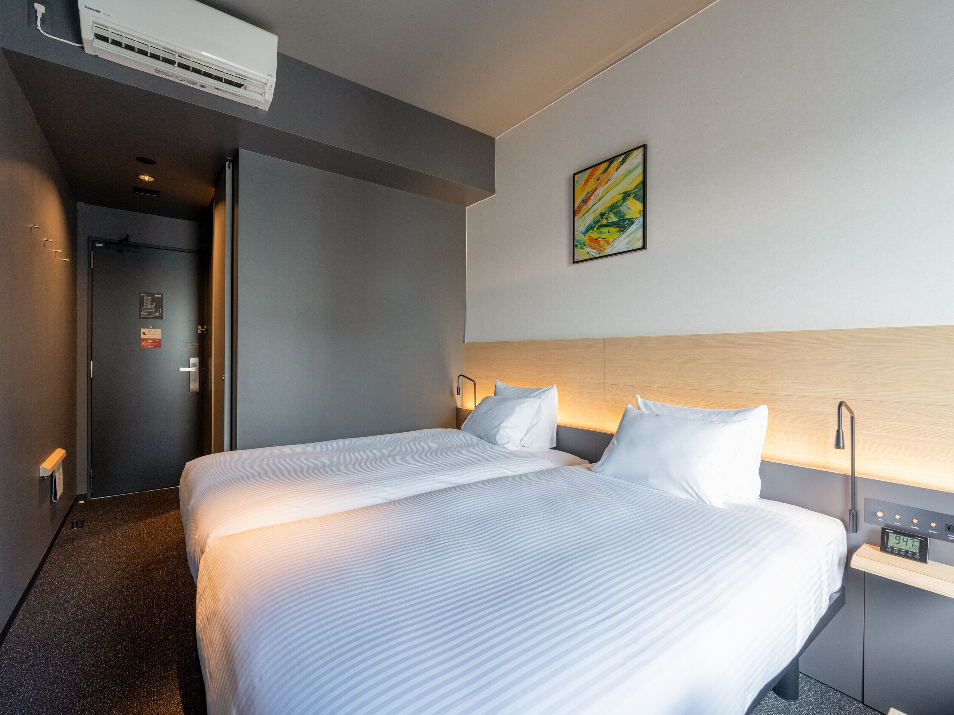Une chambre d’hôtel moderne avec un grand lit, des tables de chevet, un climatiseur fixé au mur et un tableau.