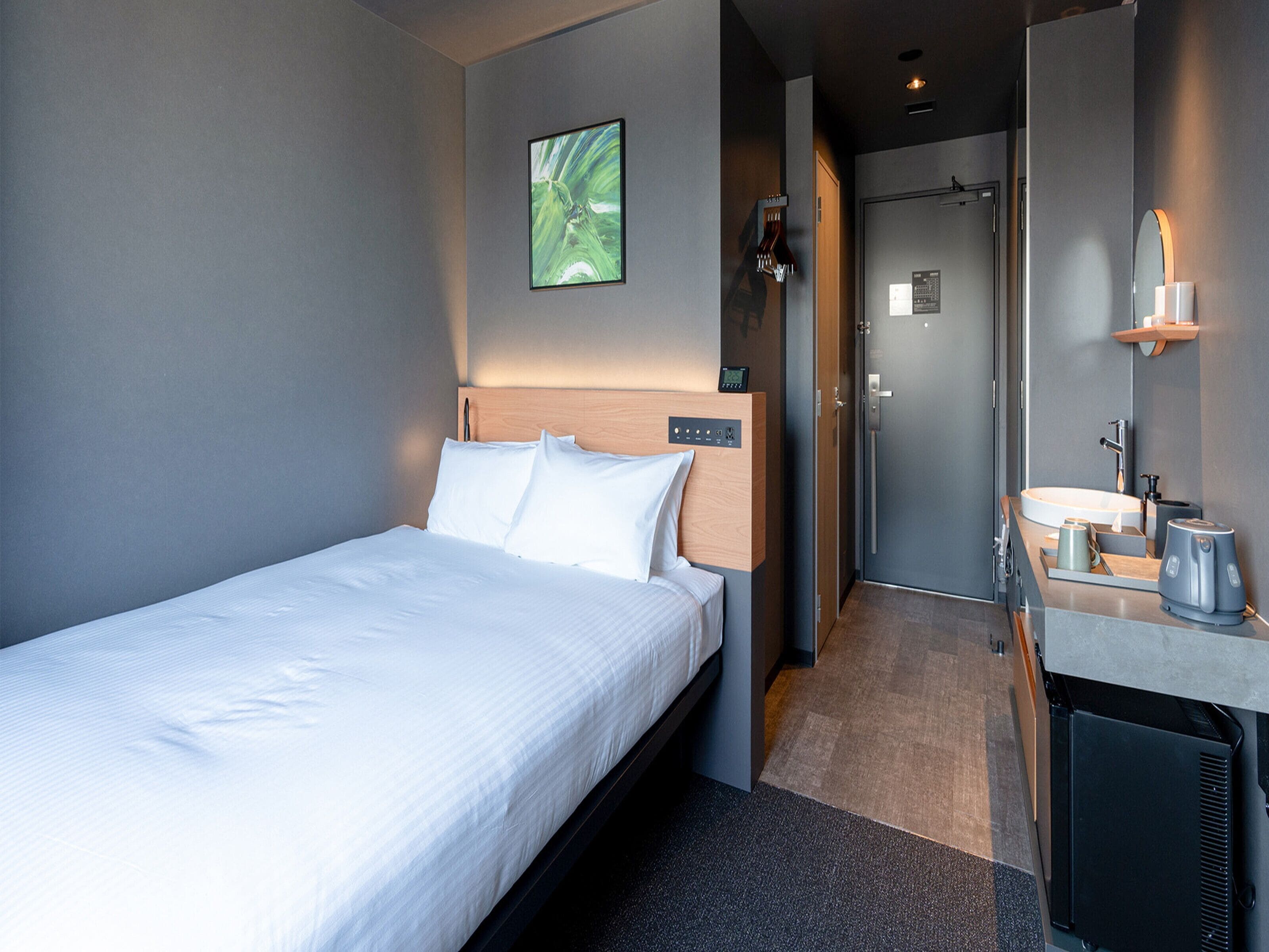 A modern hotel room with a neatly made bed, a small bathroom with a sink and mirror, and a door leading to another room.