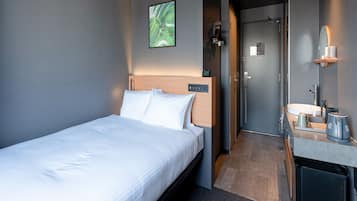 A modern hotel room with a neatly made bed, a small bathroom with a sink and mirror, and a door leading to another room.