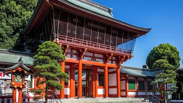 En traditionel japansk bygning med en markant rød torii-port, en overdækket gangbro og en stentrappe, der fører til indgangen.