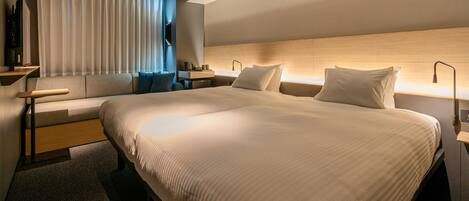 A modern hotel room with a large bed, a sofa, a desk, and a TV.
