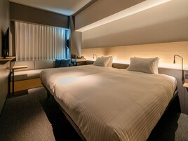 A modern hotel room with a large bed, a sofa, a desk, and a TV.