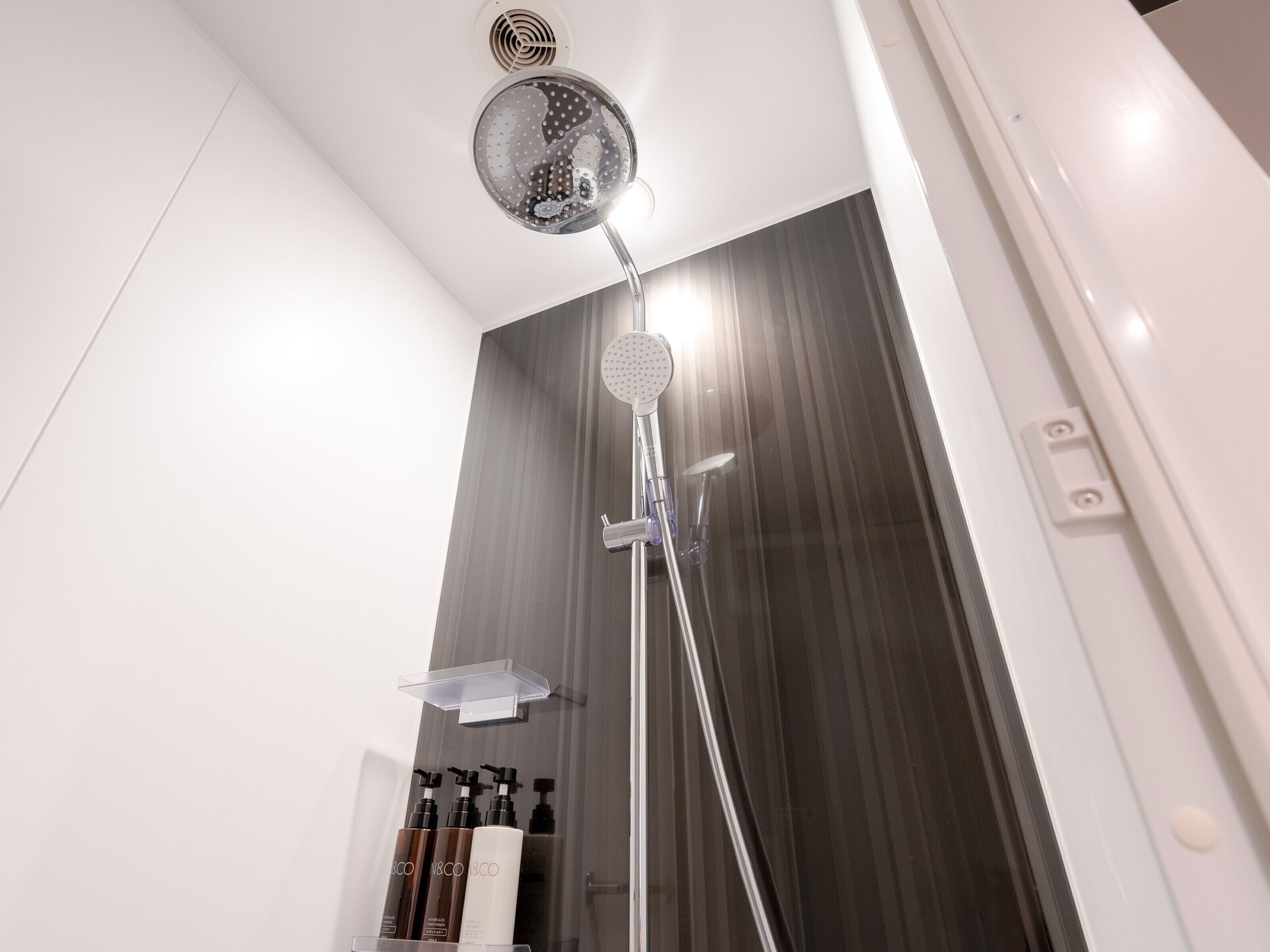 Un baño moderno con ducha, espejo y repisa con artículos de aseo.