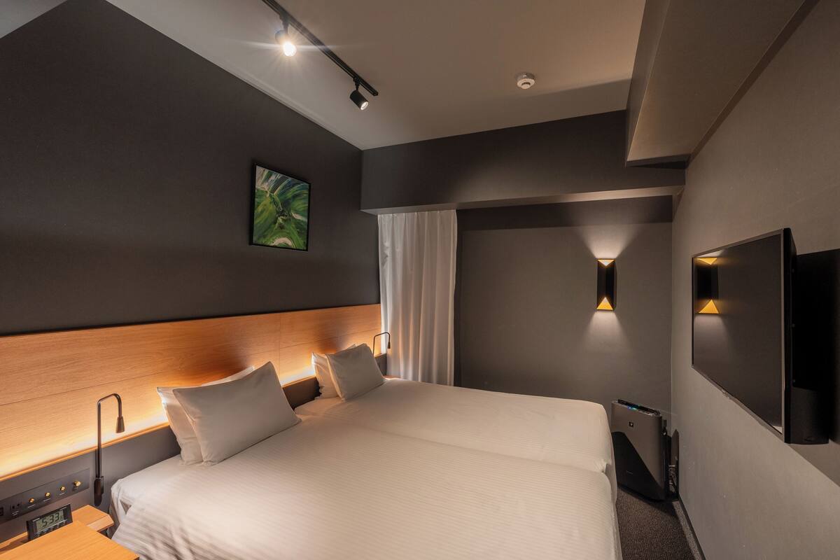 Quarto de hotel moderno com uma cama grande, mesas de cabeceira, TV de tela plana e iluminação ambiente.