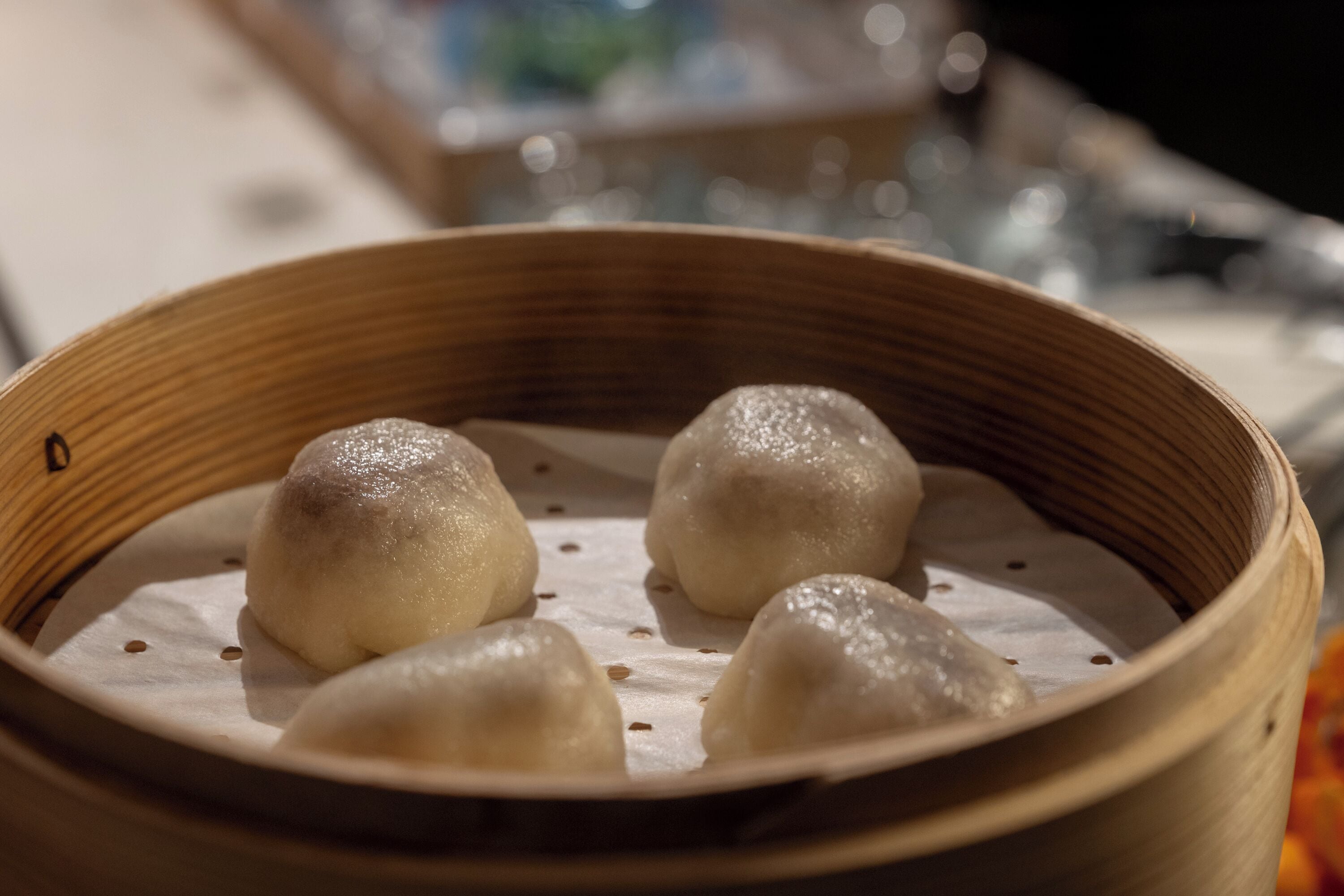 A bamboo steamer with four steamed buns.