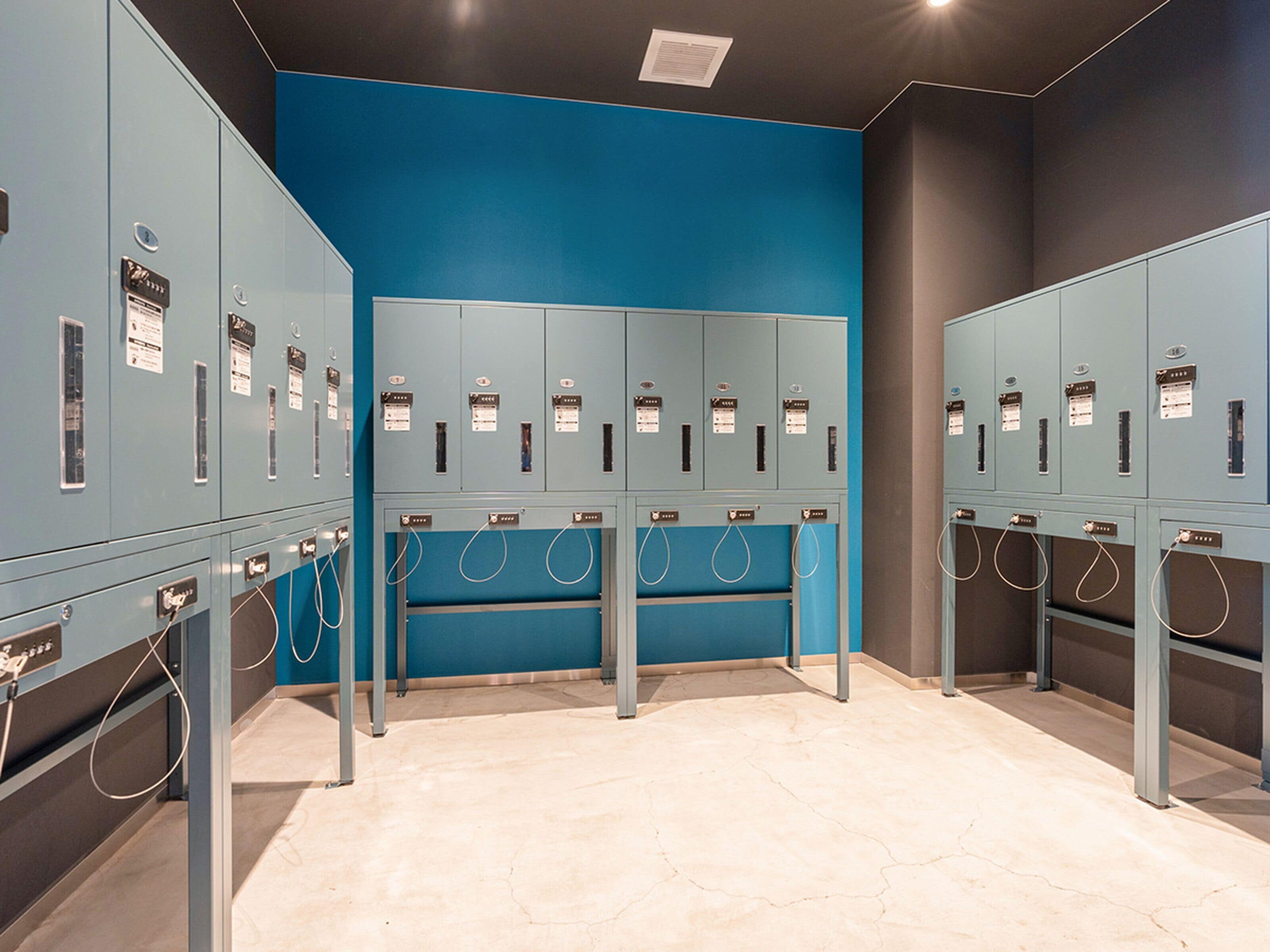 A row of lockers with a blue wall and a grey floor.