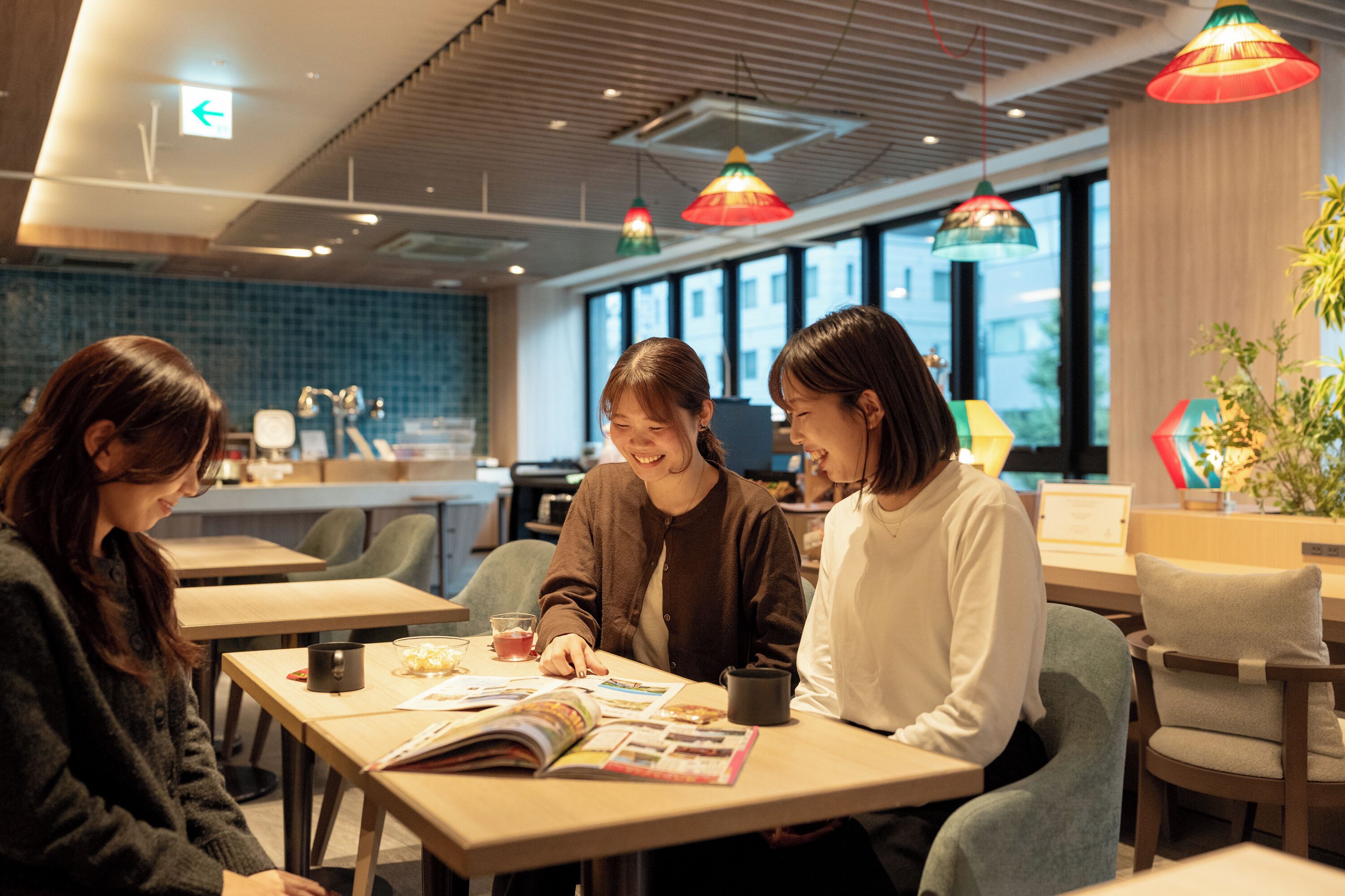 A group of people sitting at a table in a modern cafe with large windows and colorful pendant lights.
