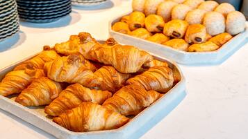Tablett mit Gebäck, darunter Croissants und kleine runde Kuchen.