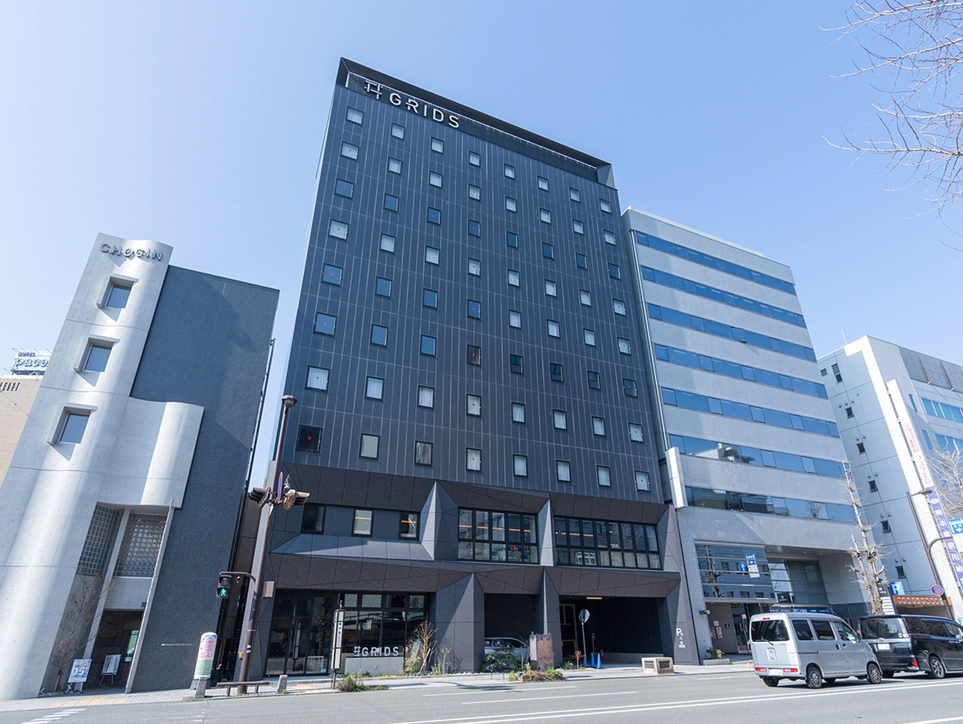 Un hotel moderno con un llamativo letrero 'GRIDS' en la parte superior, que presenta una fachada con diseño de cuadrícula y múltiples ventanas.