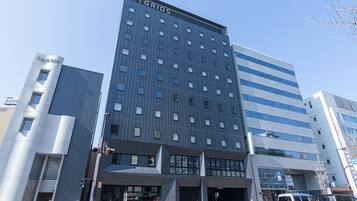 Un hotel moderno con un llamativo letrero 'GRIDS' en la parte superior, que presenta una fachada con diseño de cuadrícula y múltiples ventanas.