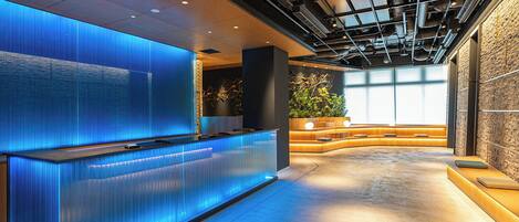 A modern reception area with a blue-lit reception desk, a large plant, and a seating area with a stone wall.