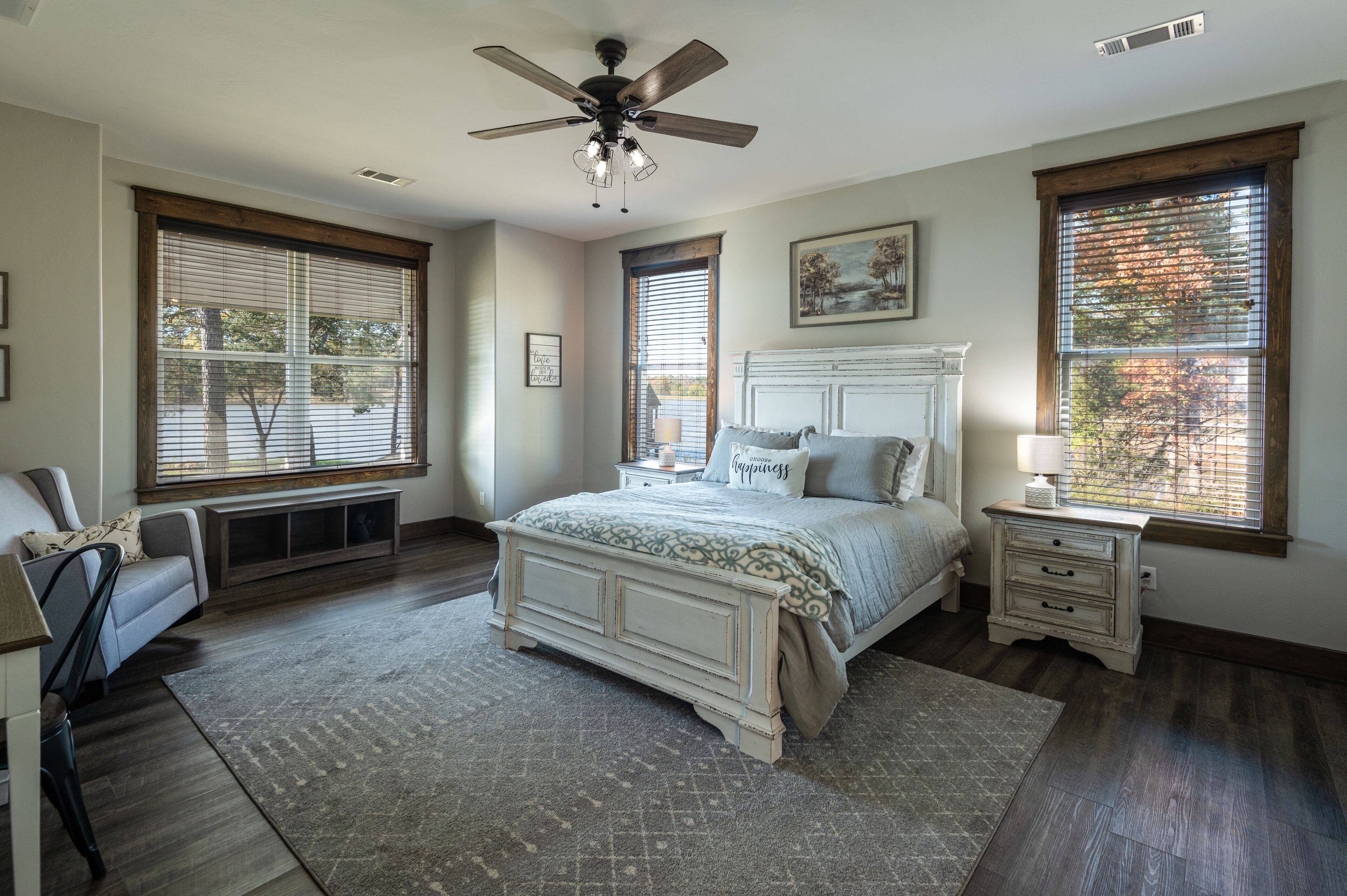 A bedroom with a large bed, a ceiling fan, and two windows with blinds.