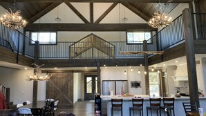A spacious interior with a high ceiling, exposed wooden beams, and a mezzanine level. - Gorgeous Mountain Lodge on Privately-Owned Lake - Sleeps 30! (Wilburton)