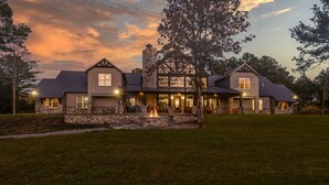 A large, two-story house with a stone facade, multiple windows, and a well-maintained lawn. - Gorgeous Mountain Lodge on Privately-Owned Lake - Sleeps 30! (Wilburton)