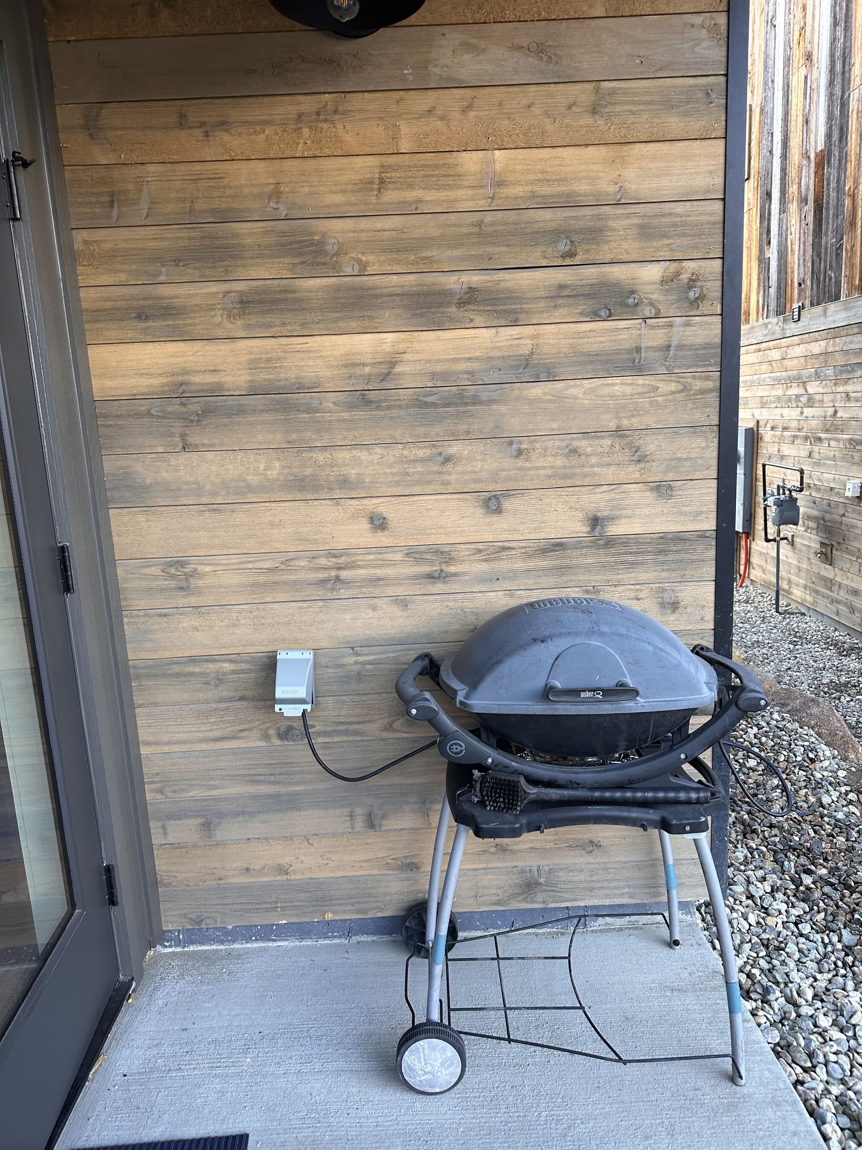 A portable grill against a wooden wall, connected to a power outlet.