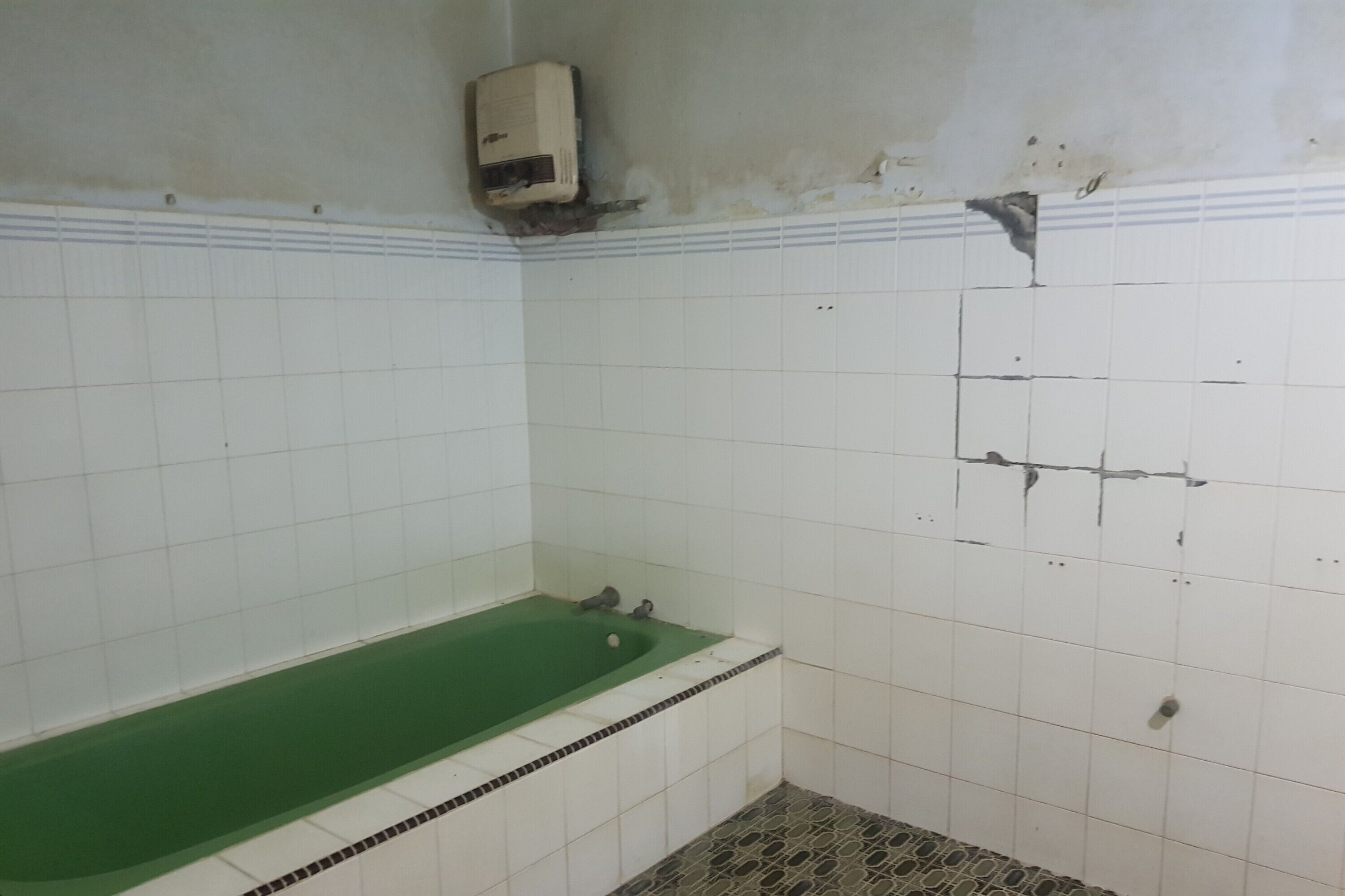 Une salle de bain avec une baignoire verte, des murs recouverts de carreaux blancs et un sol carrelé avec un motif.