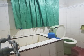 A bathroom with a green curtain, a white toilet, a blue basin, and a tiled floor. - Hotel O Triarga (Takengon)