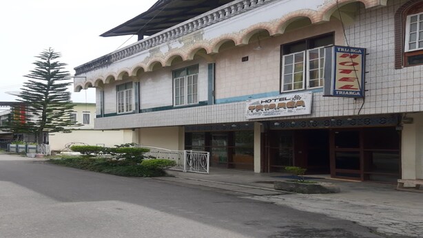 A hotel with a tiled facade, a signboard for the hotel, and a small garden area in front. - Hotel O Triarga (Takengon)