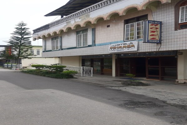 A hotel with a tiled facade, a signboard for the hotel, and a small garden area in front. - Hotel O Triarga (Takengon)