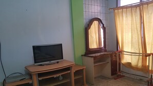 Una habitación con televisión sobre un soporte de madera, un espejo y una cortina.