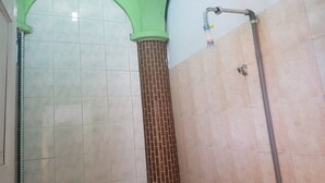 Baño con paredes de azulejos, zona de ducha y una tubería de agua a la vista.
