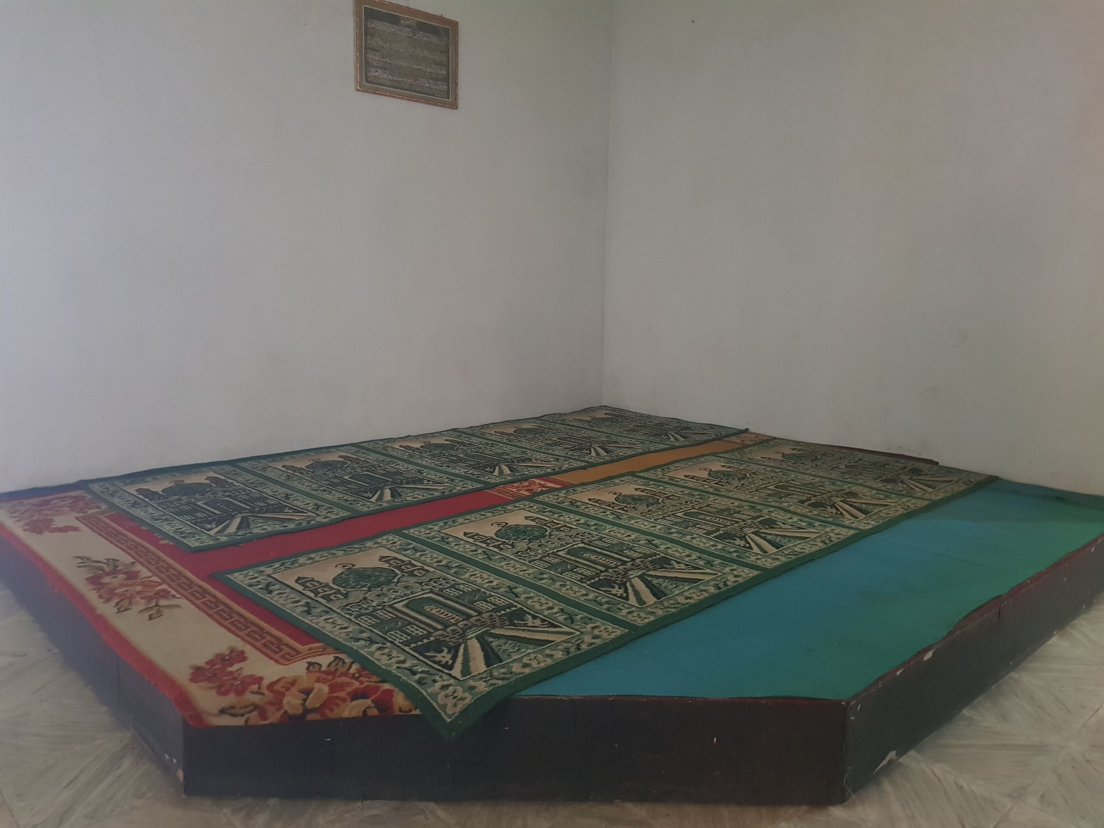 Una habitación con una cama individual, un pequeño estante en la pared y una pared blanca lisa.