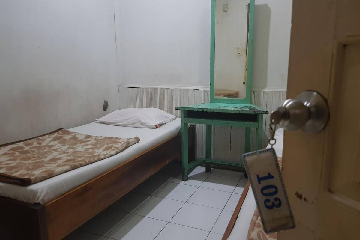Une petite chambre avec un lit simple, un bureau vert et un mur blanc.