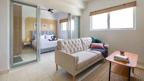 A modern hotel room with a sofa, a small table, a bed with a nightstand, and a sliding glass door leading to a balcony. - Alanis Sepang at Klia-Klia2 (Sepang)
