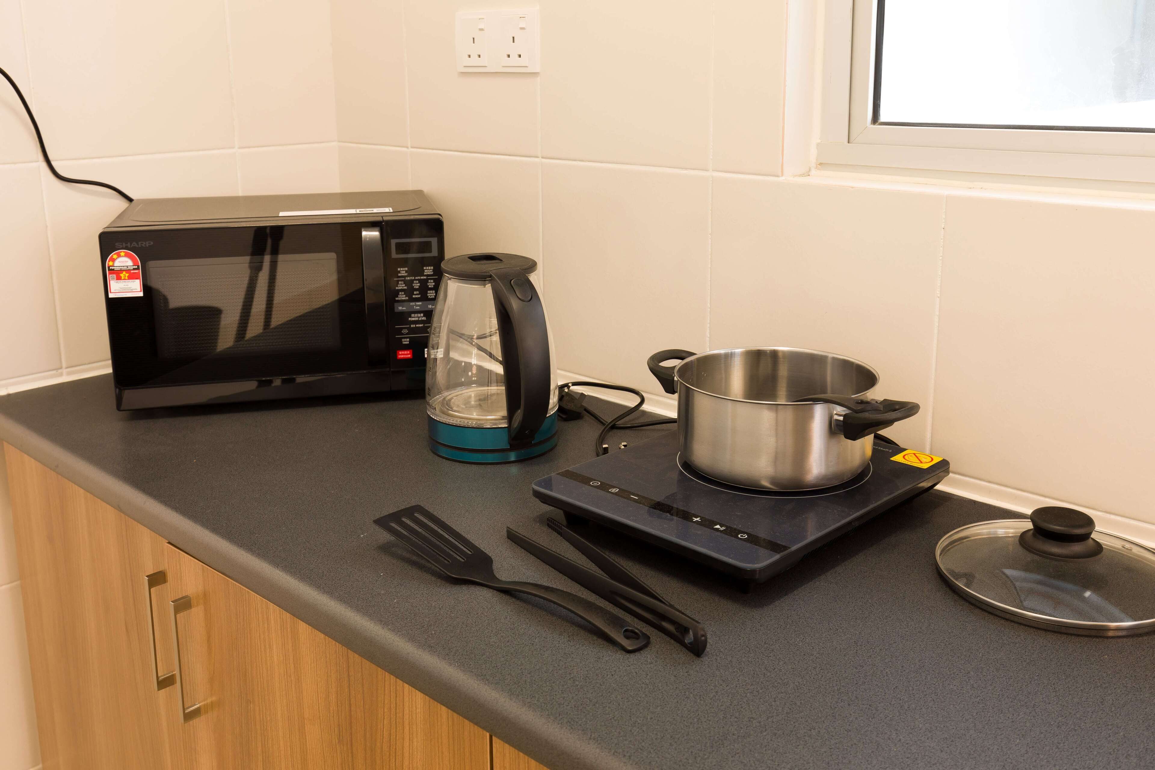A kitchen with a microwave, kettle, pot, spatula, and a stove.
