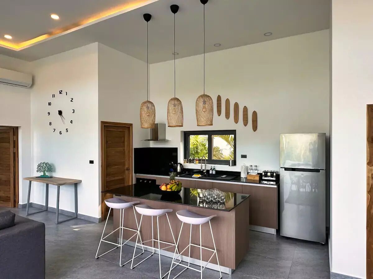 Une cuisine moderne dotée d’un îlot central, de tabourets de bar, d’un réfrigérateur en acier inoxydable et de luminaires suspendus.