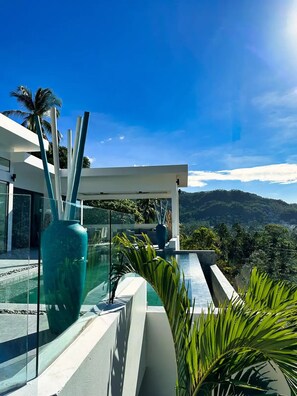 Un espace piscine extérieur moderne, doté d’une barrière en verre, d’un grand vase de couleur turquoise et offrant une vue sur une chaîne de montagnes.