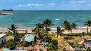 A beachfront property with a view of the ocean, palm trees, and a small building with a green roof.