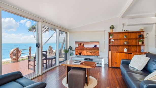 A spacious living room with a large TV, wooden furniture, and a view of the ocean.