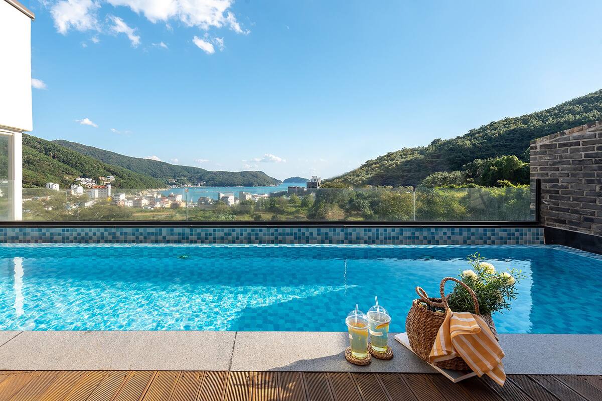 A rooftop infinity pool with a view of a coastal town and hills.