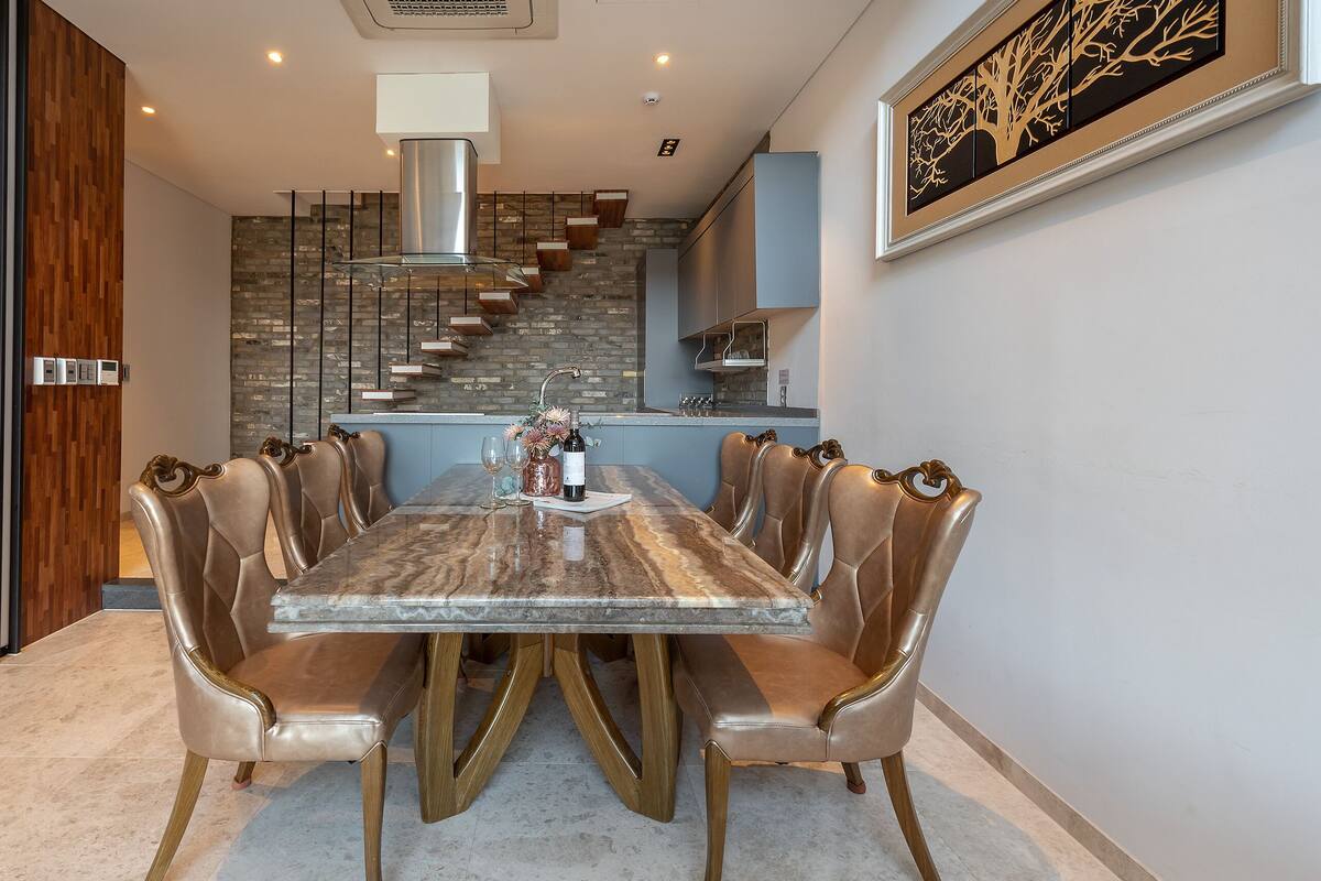 A dining area with a marble table, leather chairs, and a kitchen in the background.