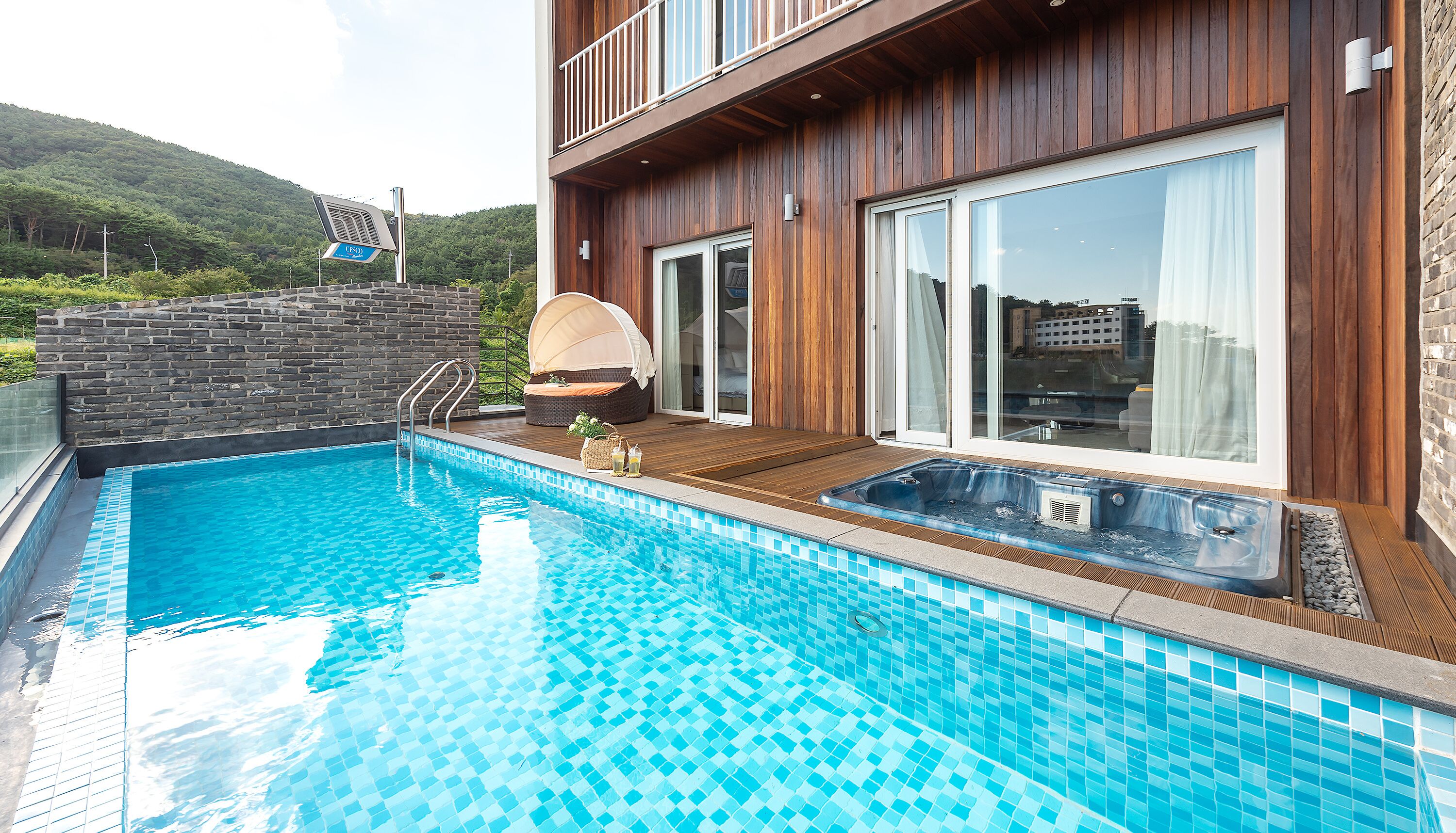 Una piscina con muelle de madera, un jacuzzi y una zona de estar techada.