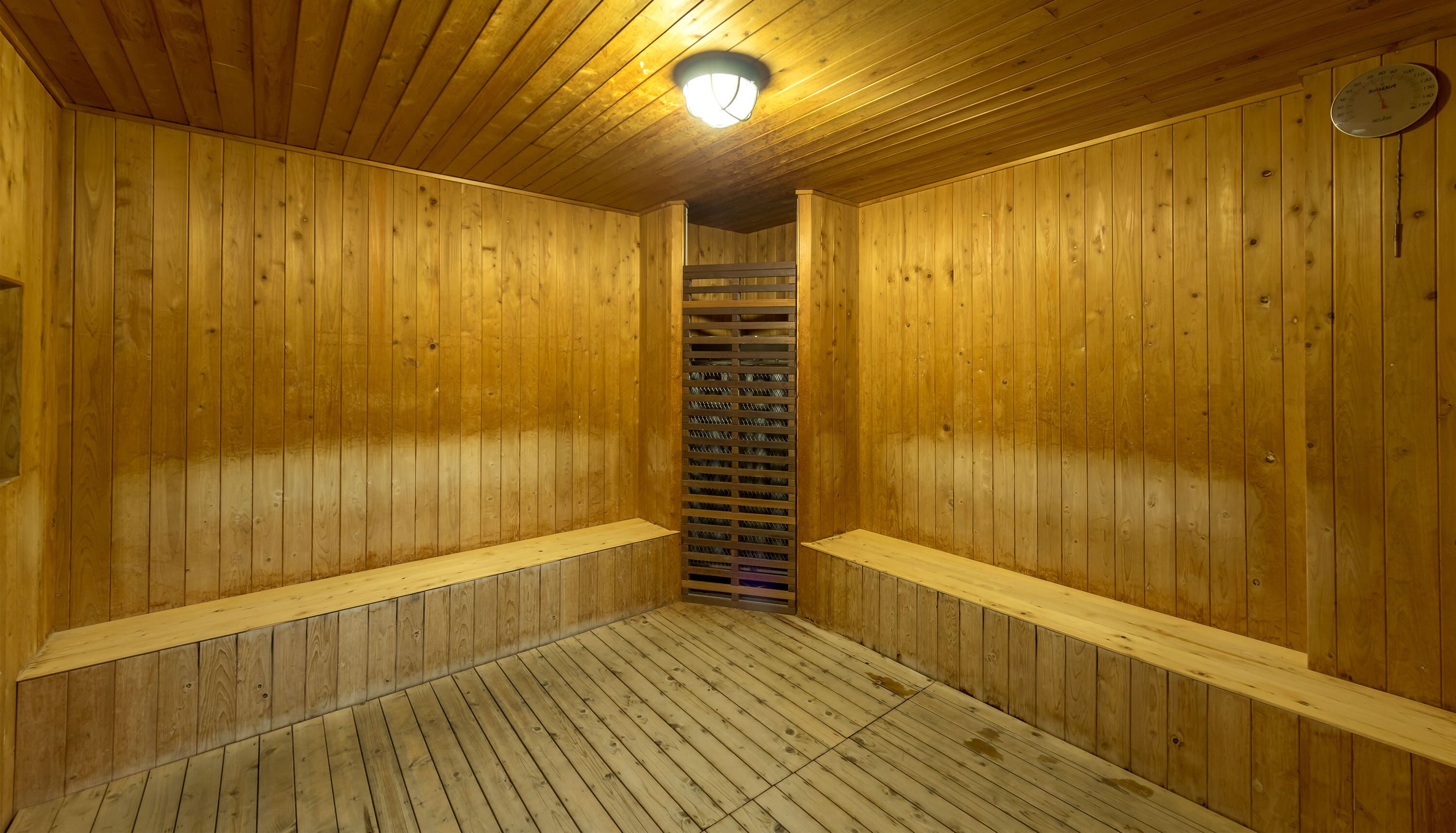 A wooden sauna with a sloped ceiling, a central ventilation grille, and a clock on the wall.