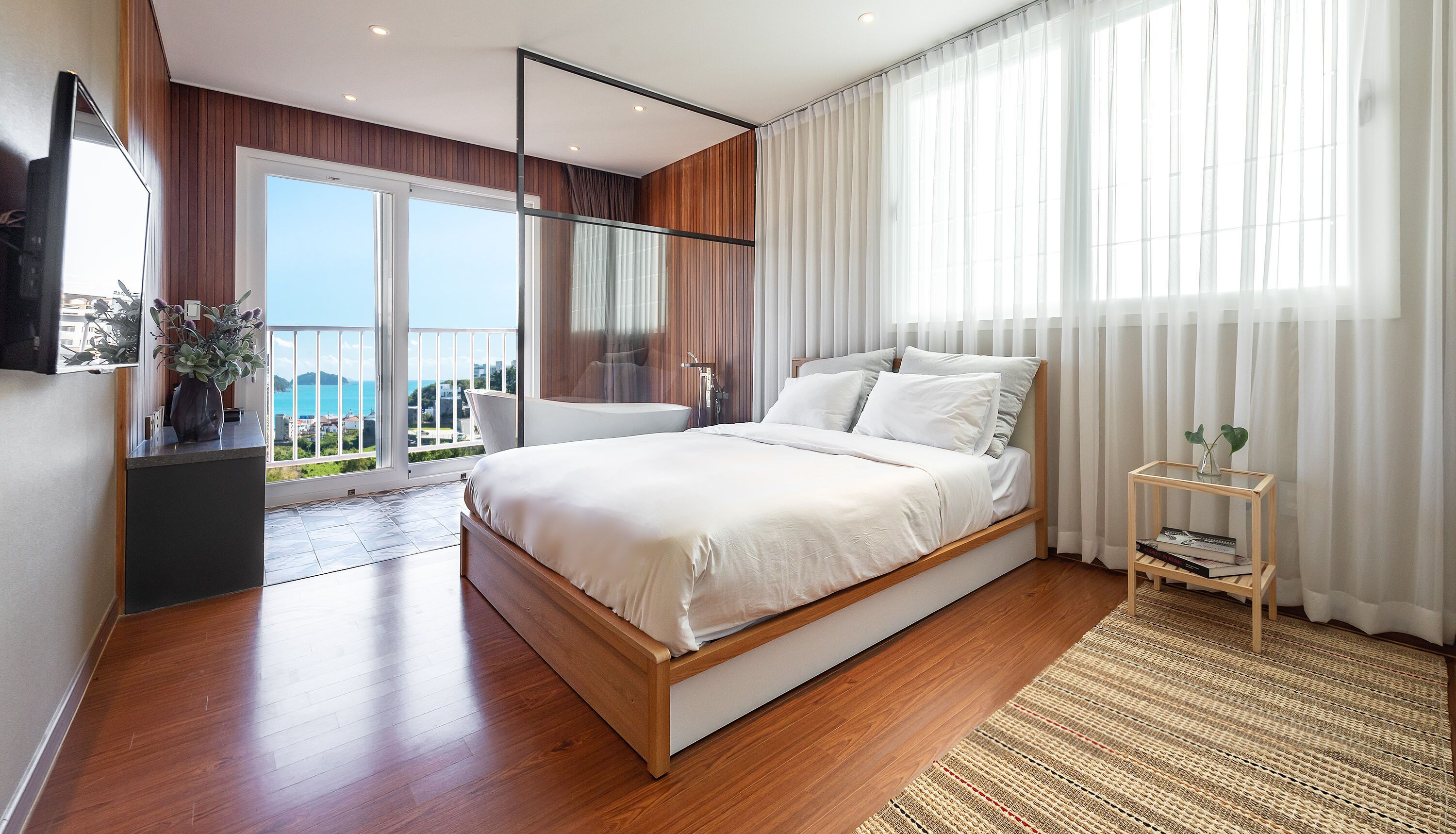 Een moderne slaapkamer met een groot bed, een balkon met uitzicht en een houten vloer.
