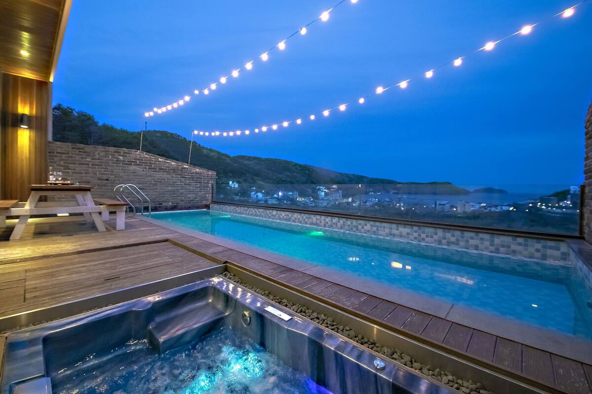 A rooftop pool area with a hot tub, wooden deck, and string lights.