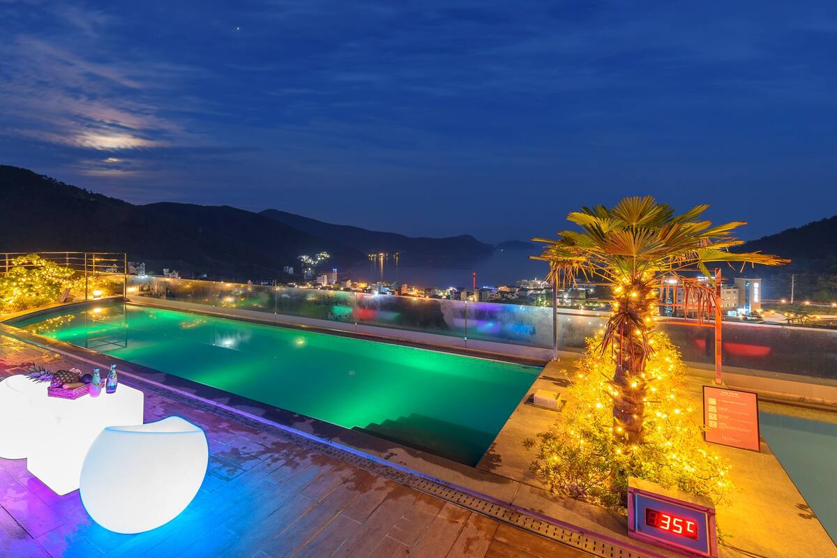 A nighttime view of a swimming pool area with illuminated seating and a digital temperature display.