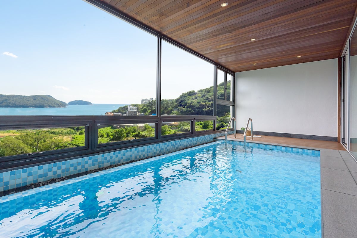 A modern indoor swimming pool with a view of the sea and hills.